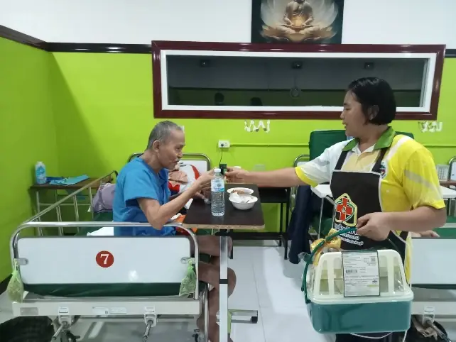 ผู้ดูแลป้อนอาหารผู้ป่วยบนเตียงในอาคารผู้ป่วย